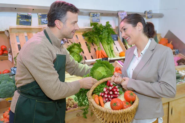 Grönsakshandlare hjälpa kunden med korg av råvaror — Stockfoto