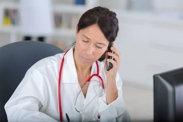 Bom olhar médico feminino no telefone em seu escritório — Fotografia de Stock