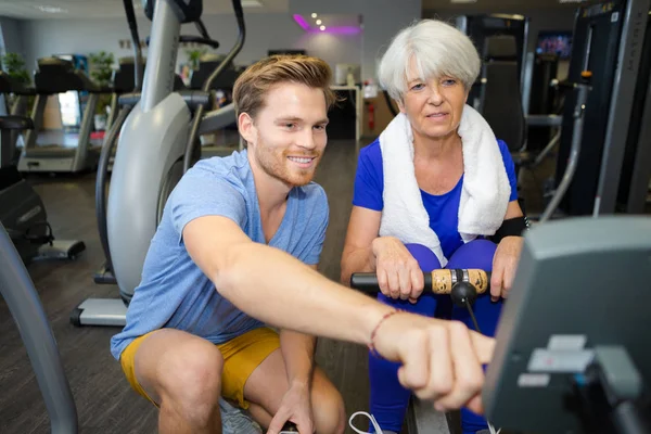 Vieja mujer feliz haciendo ejercicio en la máquina de remo en el gimnasio — Foto de Stock