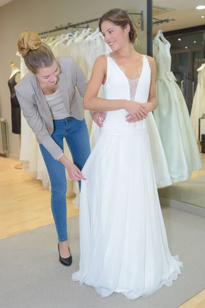 Mujer tratando de vestido de novia en una tienda con las mujeres asistente —  Fotos de Stock