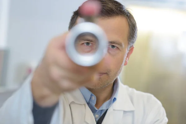 Médico masculino concentrado mirando a través de un agujero —  Fotos de Stock