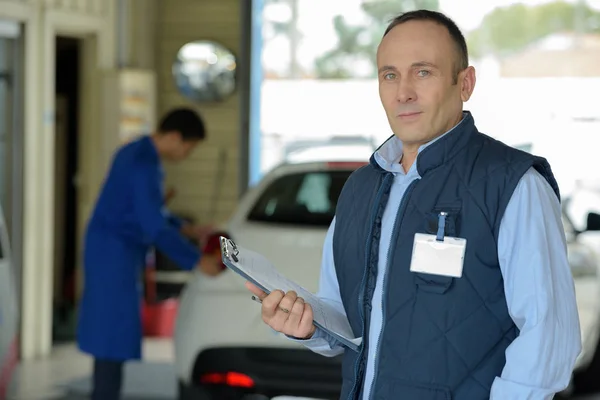 Mechaniker mit Klemmbrett und Stift steht neben Auto — Stockfoto