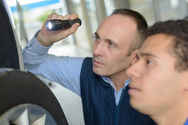 Mecânico inspecionando o carro pneu com lanterna — Fotografia de Stock