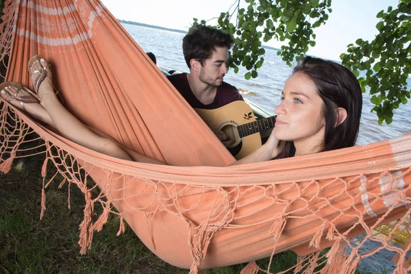 Schönes Mädchen entspannt sich in der Hängematte und hört ihrem Freund zu, wie er Gitarre spielt — Stockfoto