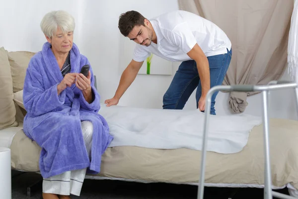 Carer preparing bed for an elderly woman — Stock Photo, Image