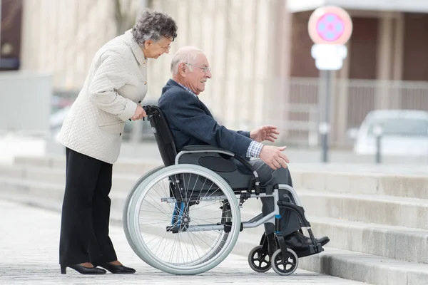 Senior homme en fauteuil roulant être poussé par femme — Photo