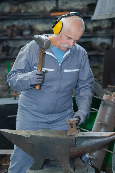 Металлообработчик с помощью молотка над наковальней — стоковое фото