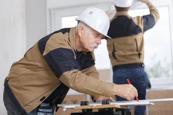 Uomo anziano falegname misure e disegna segno di matita su legno-board — Foto Stock