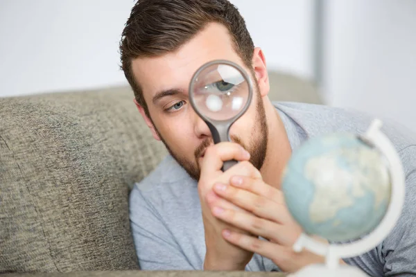 Uomo guardando il globo con una lente d'ingrandimento — Foto Stock