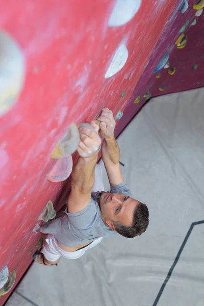 Homem alpinista na parede de escalada artificial em bouldering ginásio — Fotografia de Stock