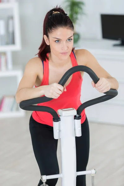 Ung kvinna gör övning på cykel hemma — Stockfoto