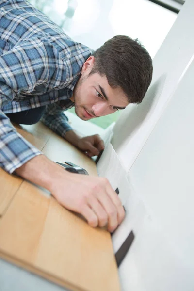 Ung man laskning laminatgolv upp mot väggen — Stockfoto