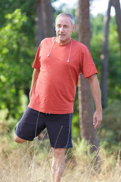 Volwassen mannelijke atleet loper die zich uitstrekt in het bos — Stockfoto