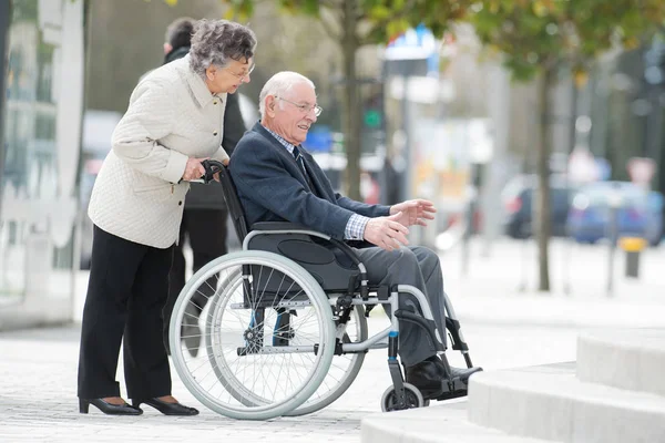 Senior dame duwen haar man in zijn rolstoel — Stockfoto