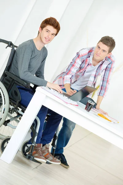 Νεαρός άνδρας σε αναπηρικό καροτσάκι στο τραπέζι με το φίλο — Φωτογραφία Αρχείου