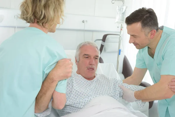 Homme plus âgé couché dans le lit d'hôpital avec des infirmières l'aidant — Photo