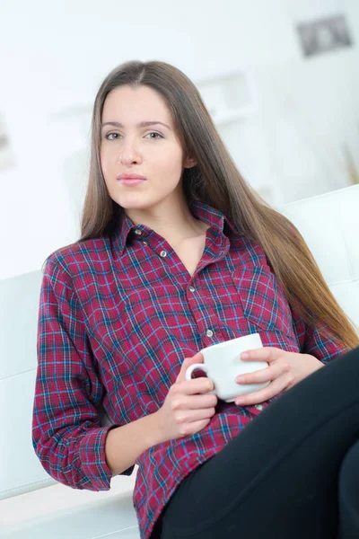 Mooie brunette met een kopje thee op een sofa — Stockfoto