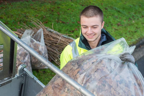 Jonge werknemers laden tas van dode bladeren in voertuig — Stockfoto
