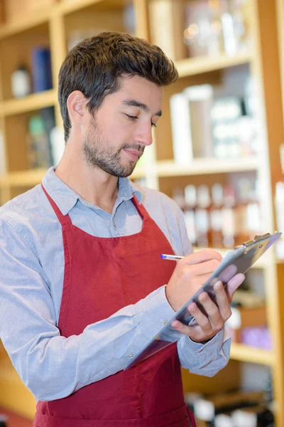 Vendedor masculino con delantal en la escritura en el portapapeles — Foto de Stock