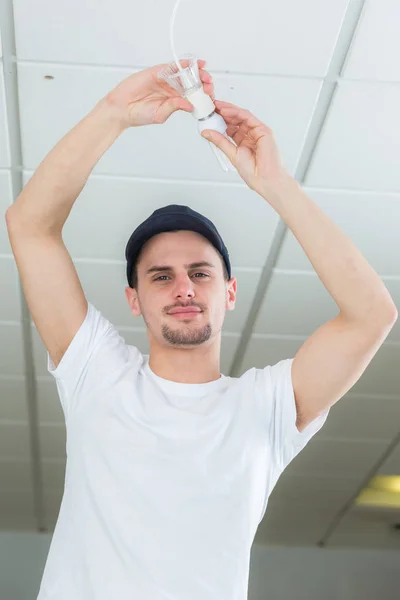 Handsome young builder installing light bulb indoors — Stock Photo, Image