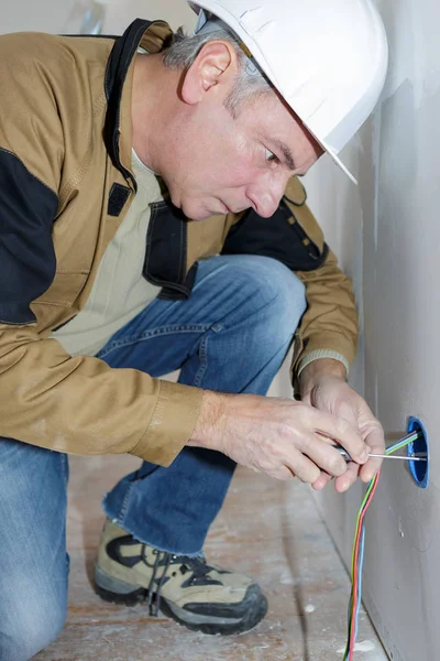 Elettricista di mezza età che ripara l'incavo elettrico sulla parete bianca — Foto Stock