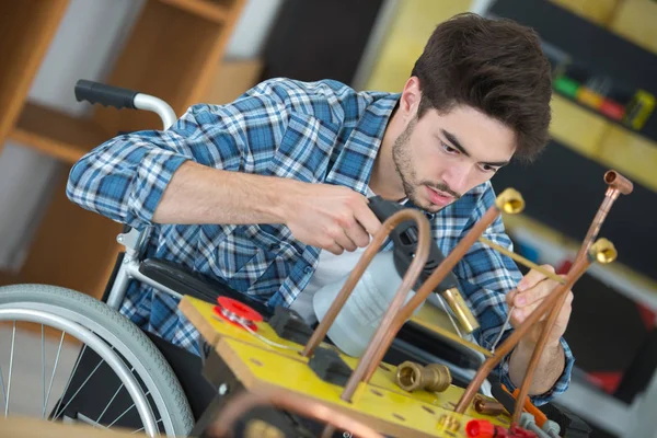 Trabajador manual en silla de ruedas que trabaja con tuberías metálicas —  Fotos de Stock