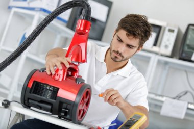 handsome young repairman fixing vacuum cleaner clipart