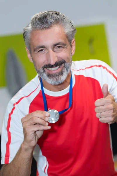 Старший мужчина показывает медаль с большим пальцем вверх — стоковое фото