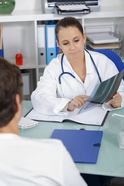 Doctor mostrando rayos X a su paciente en el consultorio médico — Foto de Stock