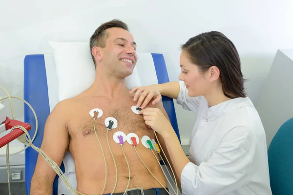 Enfermera adjuntando almohadillas de monitor cardíaco al paciente — Foto de Stock