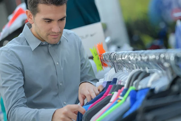 El hombre elige una camiseta en la tienda — Foto de Stock