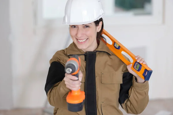 Gelukkig vrouwelijke bouwer met waterpas en elektrische boor — Stockfoto