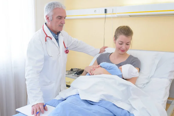 Doctor watching over mother with newborn baby in hospital bed — Stock Photo, Image