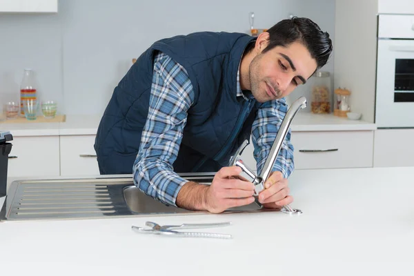 Мужчина сантехник чинит кран на кухне раковина дома — стоковое фото