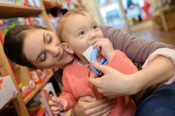 Jovem mãe sua filha fazendo compras na loja de brinquedos — Fotografia de Stock