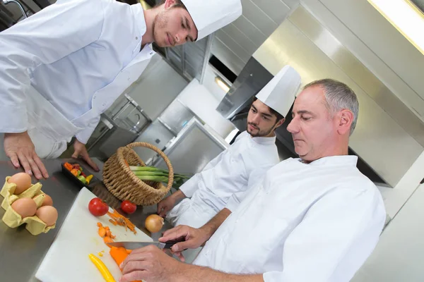 Três cozinheiros profissionais sorridentes que trabalham juntos na cozinha do restaurante — Fotografia de Stock