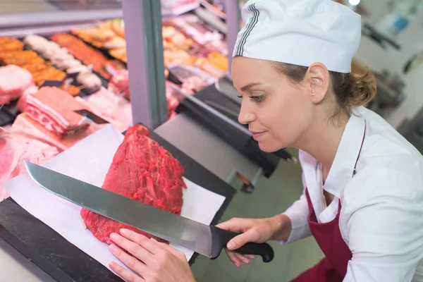 幸せな女性の肉屋精肉店カウンターで肉を切る — ストック写真