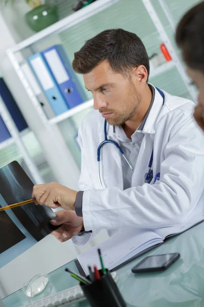 Молодой врач-мужчина показывает рентген пациенту — стоковое фото