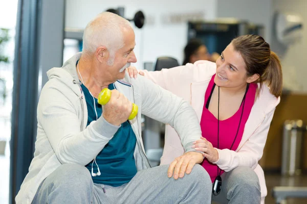 Hombre mayor haciendo ejercicio en el gimnasio con el joven instructor —  Fotos de Stock