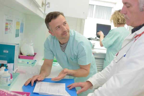 Médico e enfermeiro do sexo masculino falando sobre pasta paciente no escritório — Fotografia de Stock