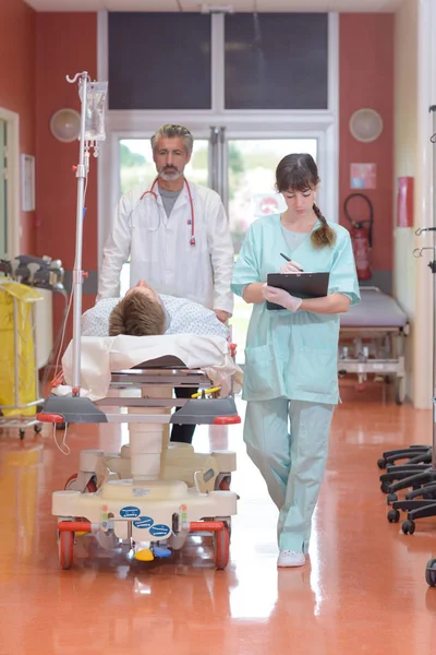 Чоловічий пацієнт на ношах штовхається через лікарняний коридор — стокове фото