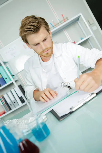 Guapo joven científico en uniforme blanco haciendo investigación en laboratorio —  Fotos de Stock