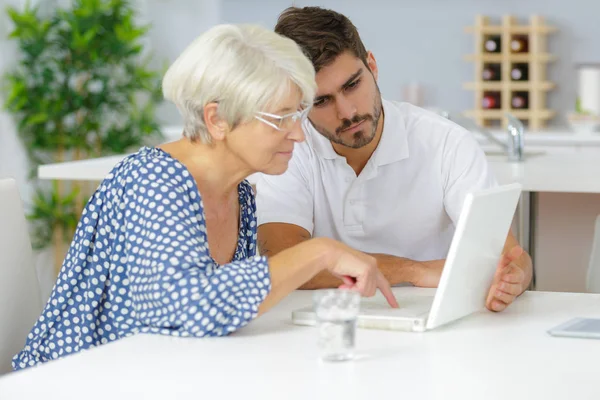 Jovem ajudando senhora sênior para usar laptop — Fotografia de Stock