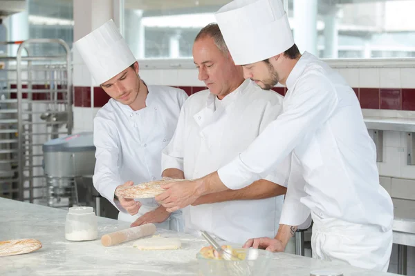 Koch mit 2 jungen Köchen in der Küche bereitet Gericht zu — Stockfoto