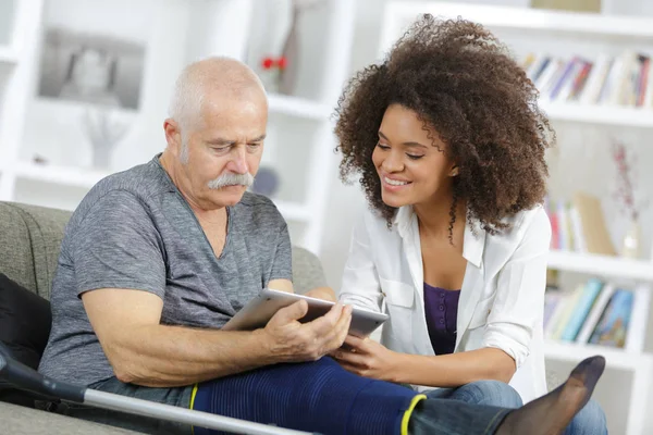 Soignant et homme âgé avec tablette assis sur le canapé — Photo