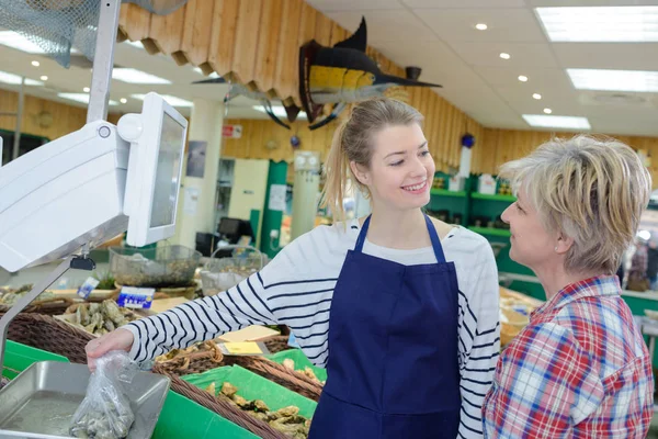 Assistente de loja feminina positiva vendendo peixe fresco e frutos do mar resfriados — Fotografia de Stock