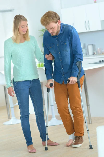 Lady helping man on crutches — Stock Photo, Image