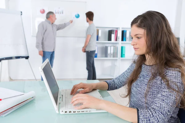 Femme étudiant tapant, les hommes au tableau blanc en arrière-plan — Photo