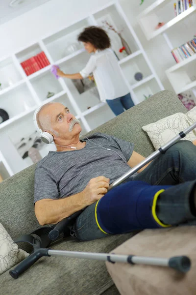 Hombre con la pierna lesionada escuchando auriculares — Foto de Stock