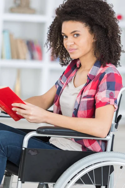 Ung kvinna sitter i rullstol läser bok — Stockfoto